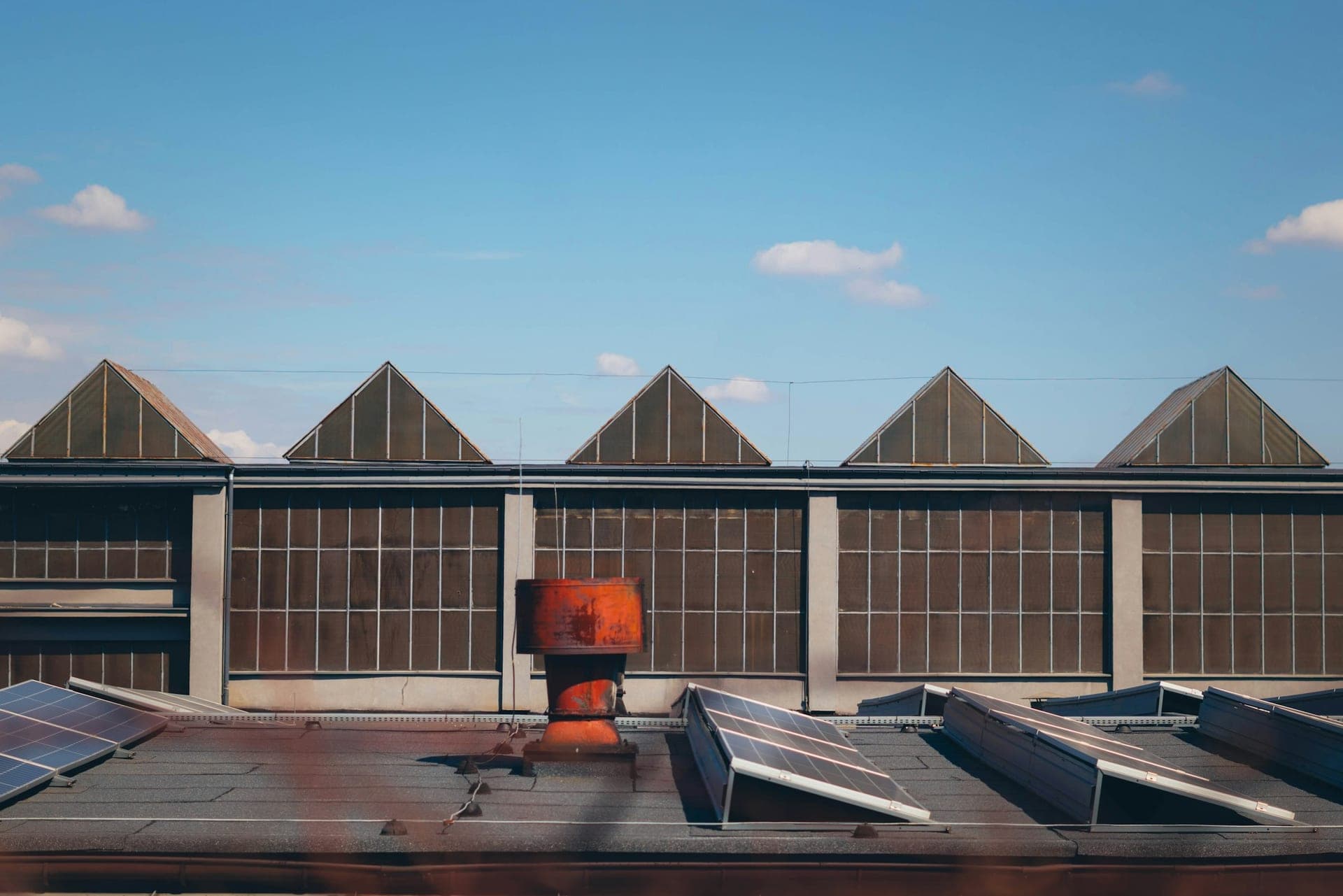 Solar panels on the flat roof of an industrial building, with a sawtooth north-light roof behind them